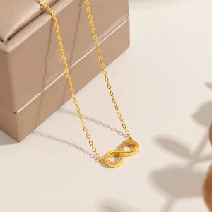 Gold infinity necklace with sparkling zircon crystals on elegant gift box background