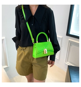 Detail of neon green crocodile texture handbag featuring metal clasp and top handle