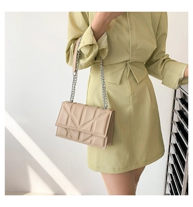 Detail of beige geometric quilted shoulder bag with silver chain strap on a model