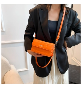 Felle oranje gewatteerde crossbodytas gedragen over een zwarte blazer en rok