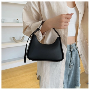 Close-up of a minimalist black matte leather underarm bag worn on a shoulder