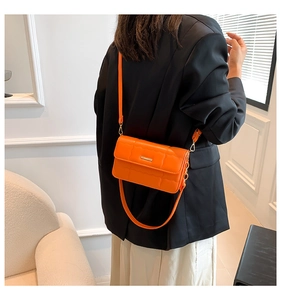 Moderne oranje gewatteerde crossbodytas gedragen door model over een zwarte blazer