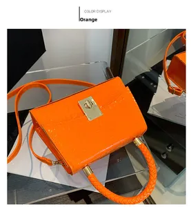 Detail of orange crocodile pattern patent leather bag with woven handle and gold metal lock