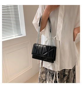 Modern black geometric crossbody bag with silver chain strap shown on a model