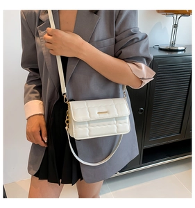 Detail van witte gewatteerde crossbodytas met gouden hardware over een grijze blazer