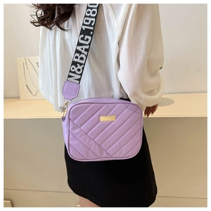 Detail of purple quilted camera bag with stylish wide woven strap and gold metal plaque