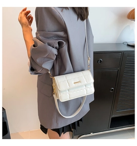 Detail van een witte gewatteerde crossbodytas met goudaccenten gedragen door een model