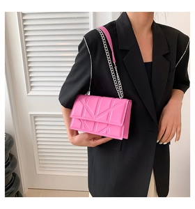 Detail of bright pink quilted crossbody bag with metal chain strap on black blazer