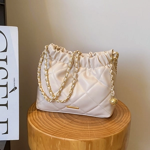 Quilted cream leather shoulder bag with gold chain strap and adjustable ball on a wood stool