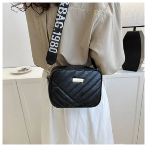 Detail of black quilted camera bag with V-shaped stitching and wide textile strap
