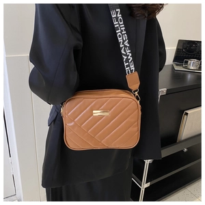 Brown quilted crossbody camera bag with wide letter-printed strap on a model