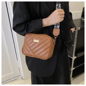 Brown quilted crossbody bag with wide jacquard strap worn by a model in casual style