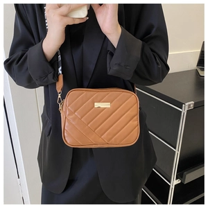 Brown quilted leather camera bag with wide patterned strap shown on a model