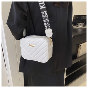 Close-up of white quilted crossbody bag with golden metal plate and wide letter strap
