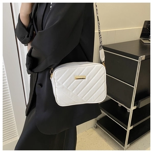 Close-up of white quilted camera bag featuring golden plate and logo woven wide strap