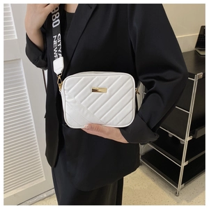 Close-up of a white quilted crossbody bag with wide woven strap and gold hardware