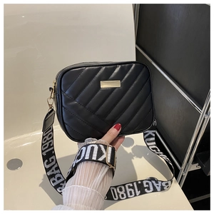 Detail of black quilted camera bag with gold metal plate and wide jacquard logo strap
