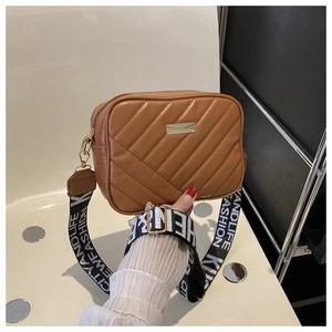 Detail of brown quilted camera bag featuring wide woven strap and gold metal hardware