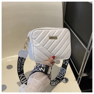 Close-up of white quilted camera bag with gold zipper and wide slogan fabric strap
