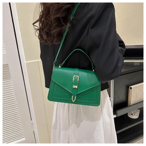 Close-up of bright green crocodile pattern bag with gold clasp held by a model