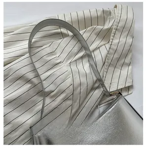 Close-up of metallic silver underarm bag with gold buckles on a striped fabric