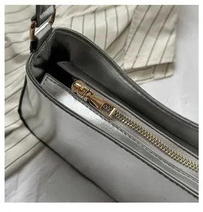 Detail of a smooth golden zipper on a silver mirror-finish shoulder bag with metallic texture