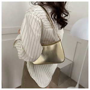 Close-up of a stylish gold mirrored shoulder bag worn by a model in a modern interior