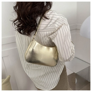 Detail view of a gold metallic hobo bag worn with a striped shirt in a minimalist room