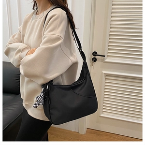 Détail d'un sac bandoulière noir en demi-lune avec un petit charm pochette à damier chic