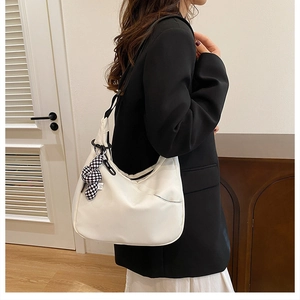 Sac hobo blanc avec large bandoulière noire et breloque damier porté à l'épaule