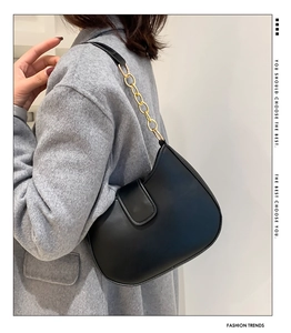 Détail du sac sous le bras noir avec chaîne dorée porté sur un manteau en laine chic