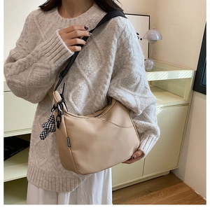 Détail d'un sac demi-lune beige avec bandoulière noire et breloque en damier