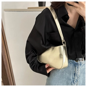 Close-up of glossy metallic gold shoulder bag with sleek curved silhouette and zipper