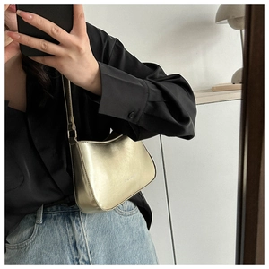 Mirror selfie showing a glossy gold metallic underarm bag with a sleek crescent design