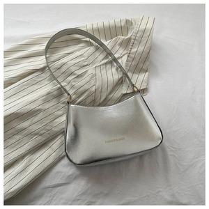 Close-up of metallic silver underarm bag with gold printed logo on striped background