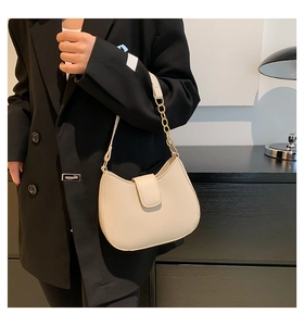 Détail du sac selle crème avec bandoulière chaîne dorée sur une veste noire