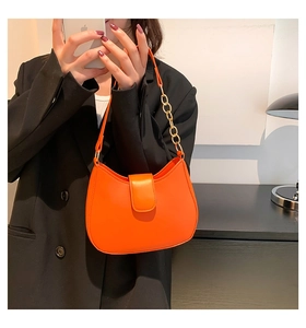 Détail du sac croissant orange vif avec chaîne dorée porté sur un blazer noir élégant