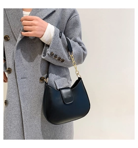 Détail d'un sac bandoulière chic en cuir brillant noir avec chaîne dorée sur un manteau