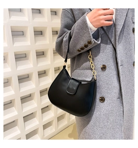 Détail d'un sac demi-lune noir avec chaîne dorée porté sur un manteau de laine gris