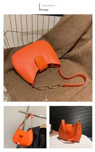 Détail du sac orange en forme de lune avec chaîne dorée et texture cuir lisse