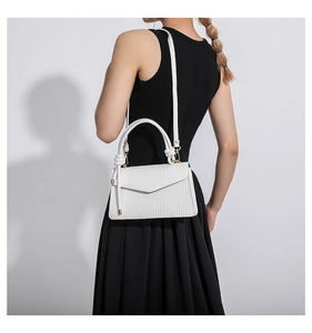 Detail of white crossbody bag with woven texture, round handle, and knot detail on model