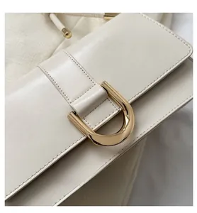 Close-up of cream PU leather flap bag with gold D-ring buckle and stitching detail