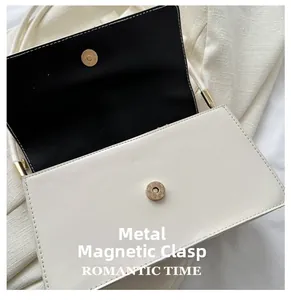 Detail of the golden magnetic buckle closure on a white leather shoulder bag