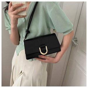 Close-up of black leather crossbody bag with golden buckle on light green knitwear