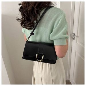 Detail view of a black minimalist shoulder bag with a gold horseshoe clasp and knotted strap