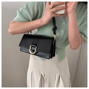 Detail of a chic black leather crossbody bag with a gold U-shaped buckle on a model