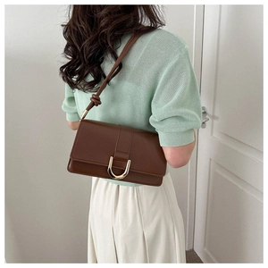 Detail of dark brown leather crossbody bag with U-shaped gold buckle and knotted shoulder strap