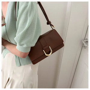 Close-up of brown leather crossbody bag with golden U-shaped buckle on green knitwear