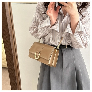 Detailed view of brown leather crossbody bag with gold U-shaped metal buckle and strap