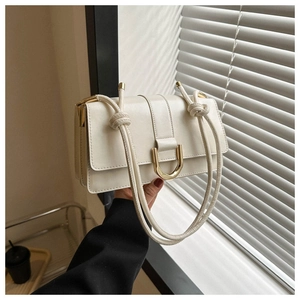 Detail of minimalist beige shoulder bag with golden U-shaped lock and knotted strap